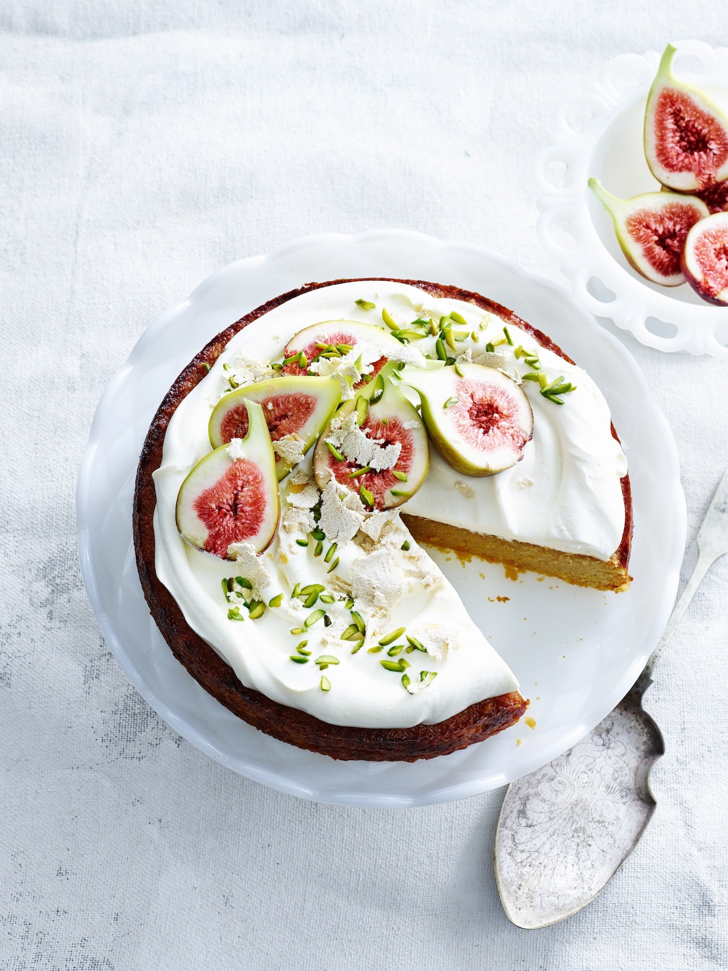 overhead-view-of-orange-and-almond-cake-with-yoghurt-cream-pistachios-figs-and-cake-server.jpg